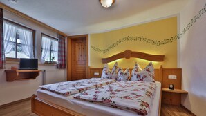 A bedroom with a wooden bed, a nightstand, a wall-mounted shelf, and a window with curtains.