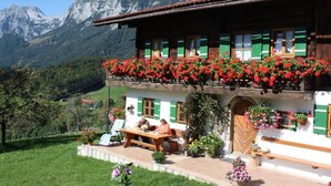 A traditional chalet with a balcony adorned with red flowers, a wooden table, and a bench outside.