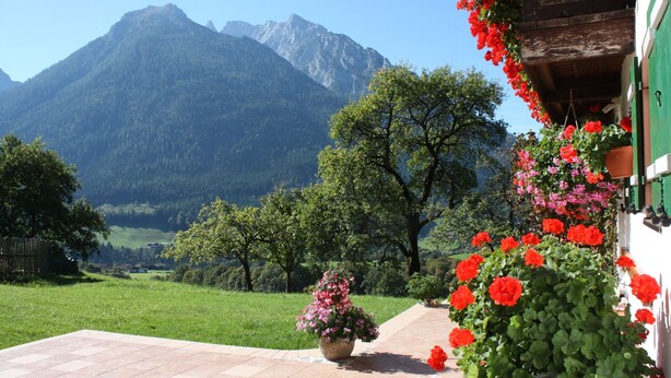 A patio with a view of mountains, a wooden building with flower boxes, and a tiled floor.