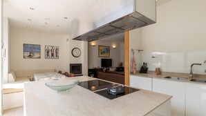 Eine moderne Küche mit Kochinsel, ein Essbereich inklusive Sofa und ein Wohnzimmer mit Fernseher und Kunstwerken.