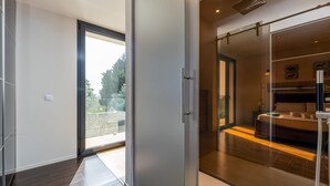 Ein modernes Hotelzimmer mit Glastür zu einem Balkon, einem Bett und einem Badezimmer mit Dusche.