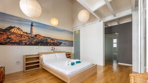 Ein Schlafzimmer mit einem hölzernen Bett, einem Gemälde einer Küstenszene und einer Toilette im angrenzenden Raum.