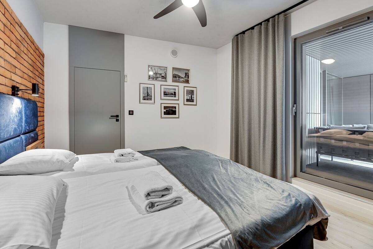 A modern hotel room with two beds, a large window with a view, and a brick accent wall.