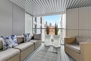 A balcony with a wicker sofa, two white vases, and a view of buildings.