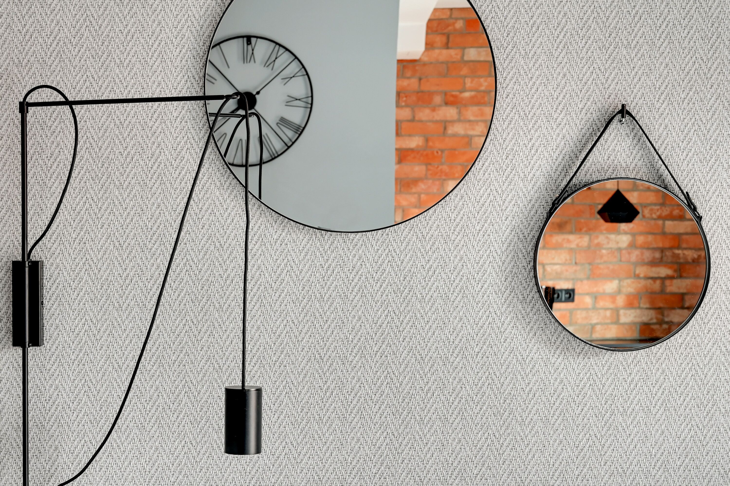A wall with a textured pattern, a circular clock, and a hanging mirror reflecting a brick wall.