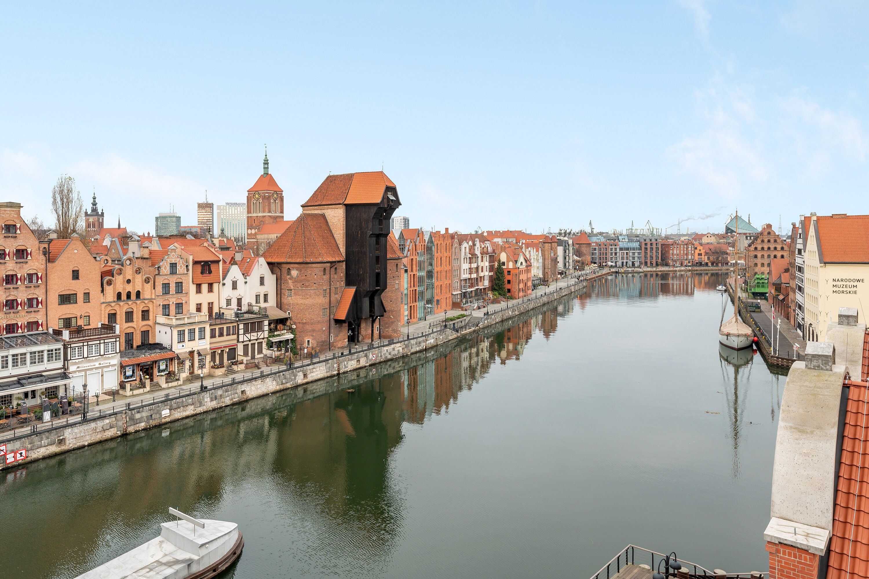 A river with buildings on both sides, a bridge in the distance, and a boat docked on the river.