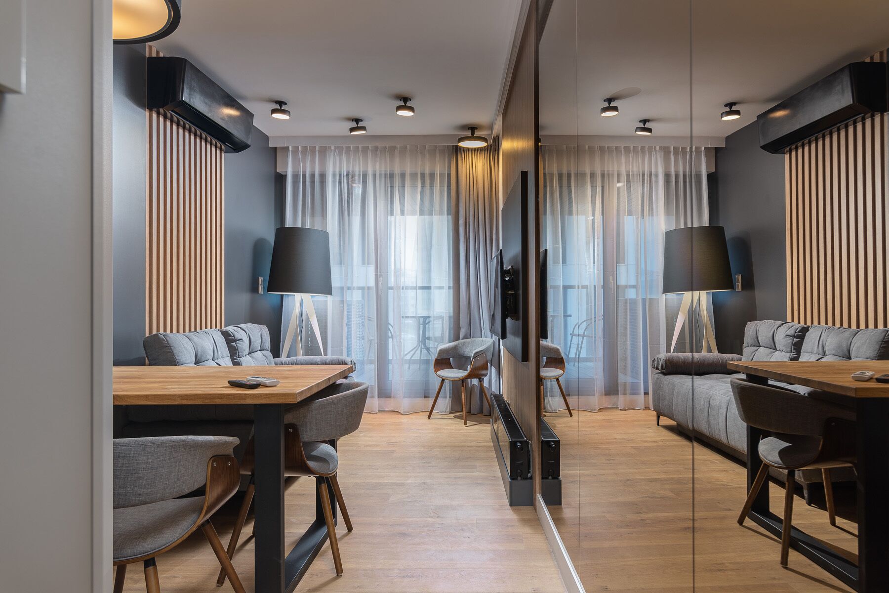 Et moderne hotelværelse med sofa, stole, et fjernsyn og et stort spejl.