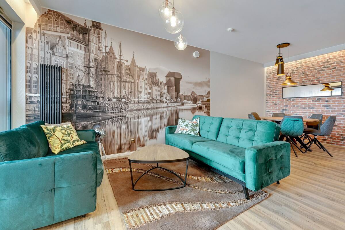 A modern living room with a large mural, teal sofas, a round coffee table, and a brick accent wall.