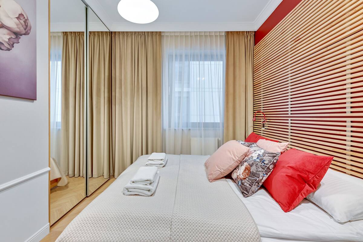 A modern hotel room with a large bed, beige curtains, a wooden headboard, and a view of the outdoors.