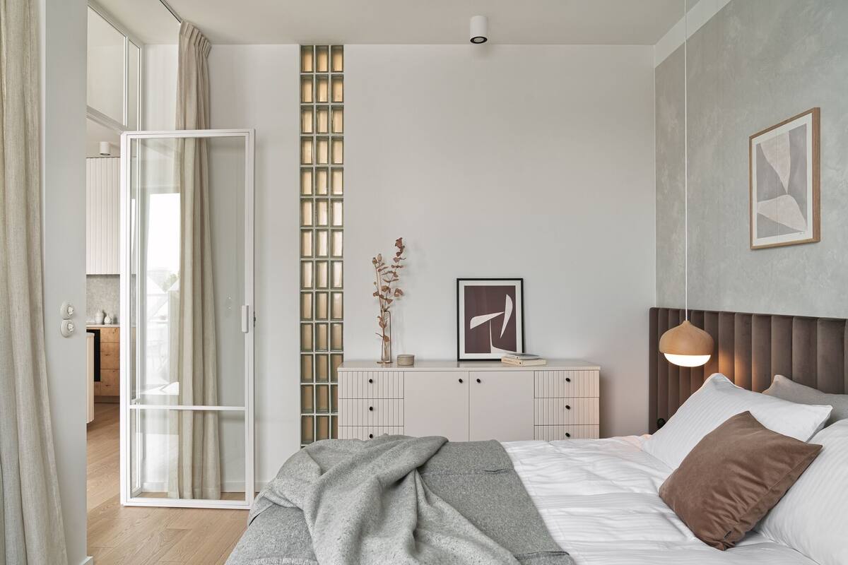 A bedroom with a bed, bedside table, and a view of a kitchen.