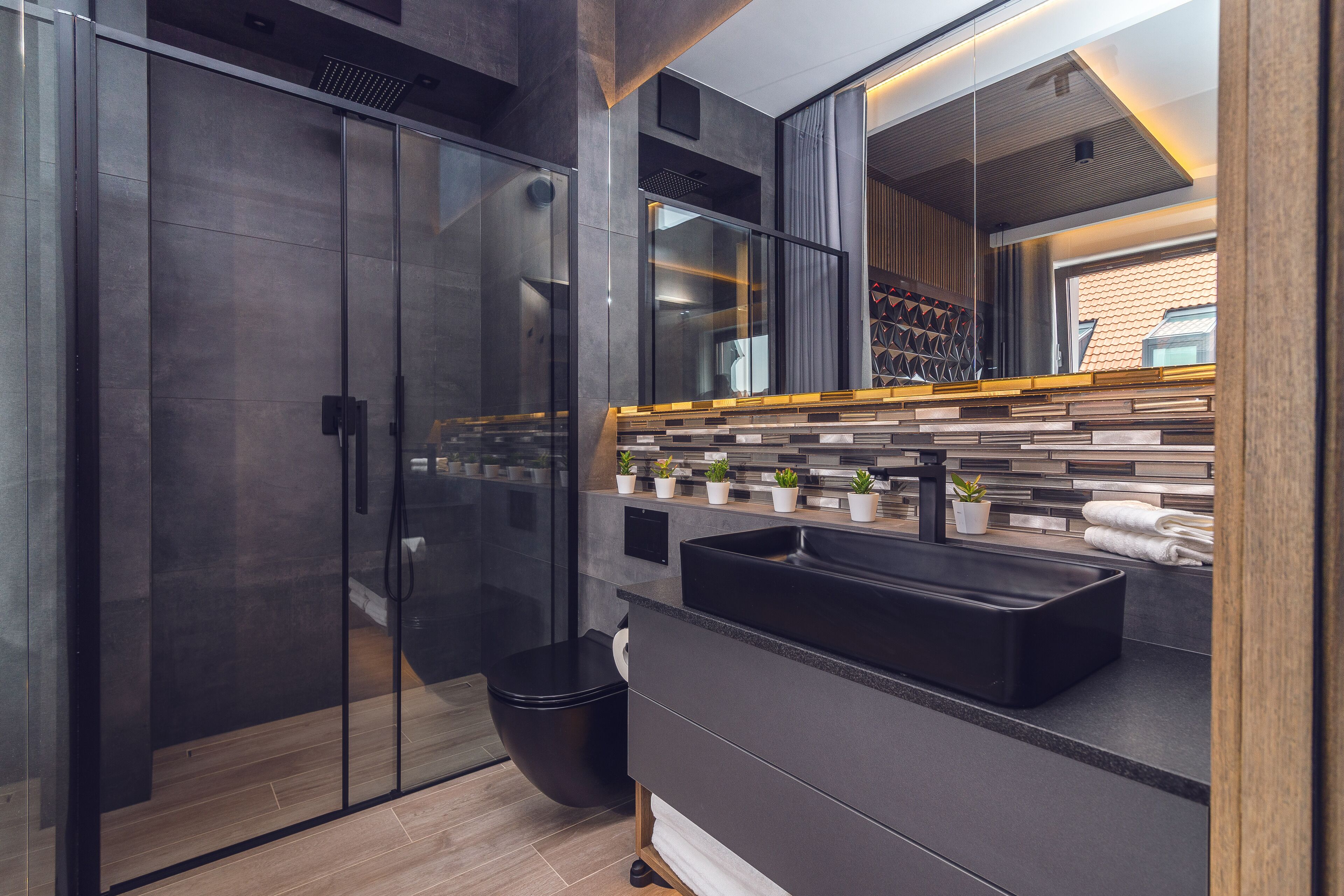 Une salle de bain moderne avec une douche à parois de verre, un lavabo noir et un miroir au-dessus du plan de toilette.