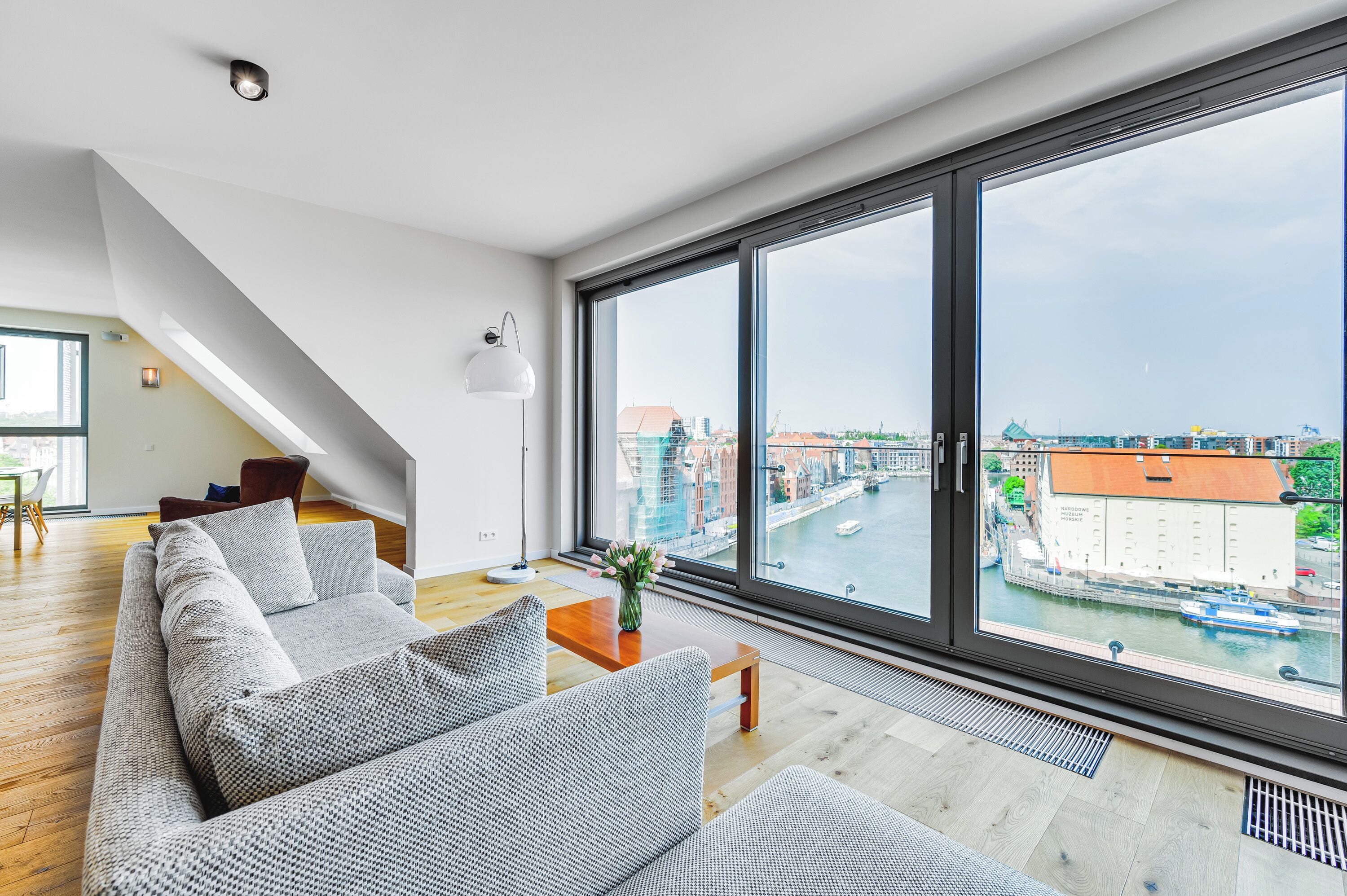 A modern living room with a large window, a sofa, a coffee table, and a staircase.