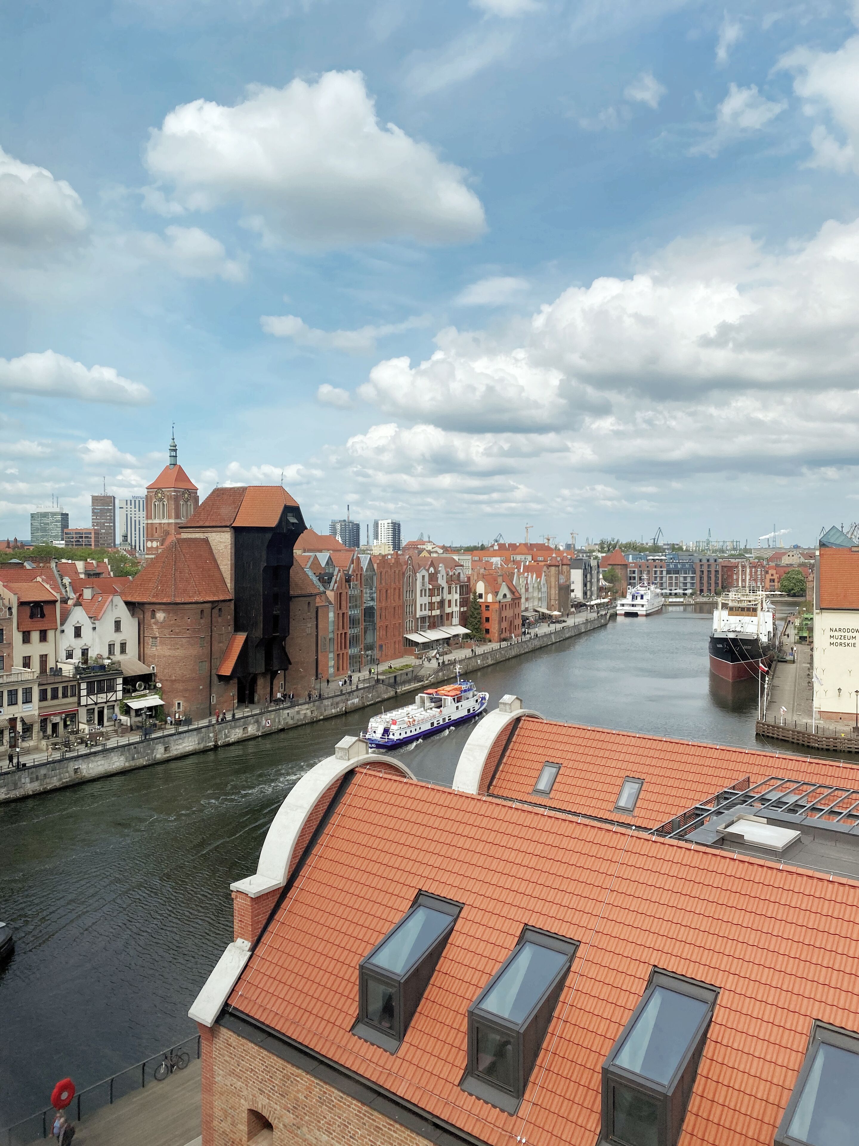 A river with boats, a bridge, and buildings with red roofs.