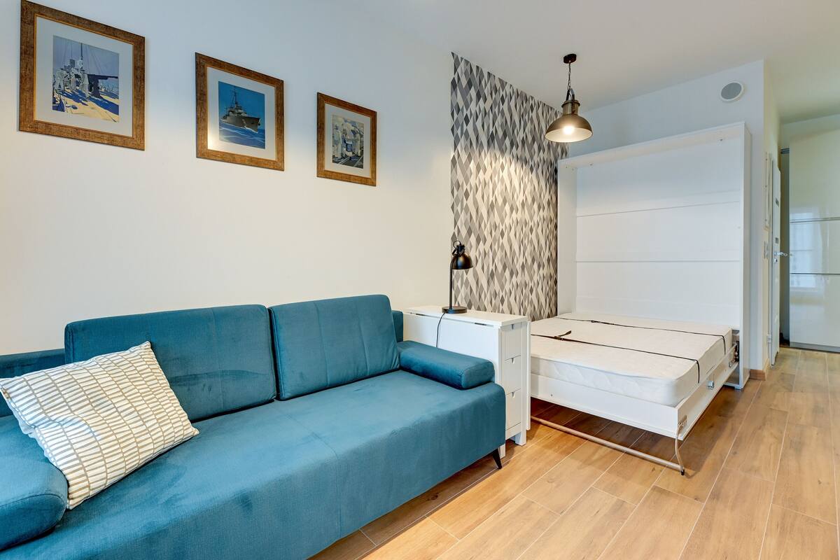 A modern room with a blue sofa, a white bed, and three framed pictures on the wall.