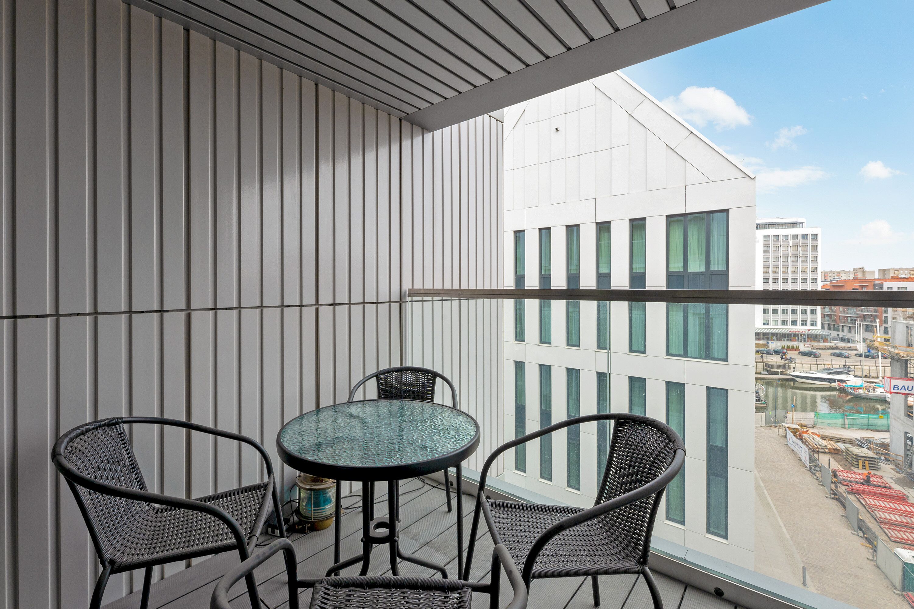 Ein Balkon mit Tisch und Stühlen, Blick auf eine Stadtansicht, und ein Gebäude mit weißer Fassade und grünen Fenstern.