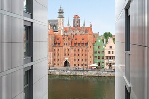 A view of a historic building with a red-tiled roof and a tower, adjacent to modern buildings with vertical lines.