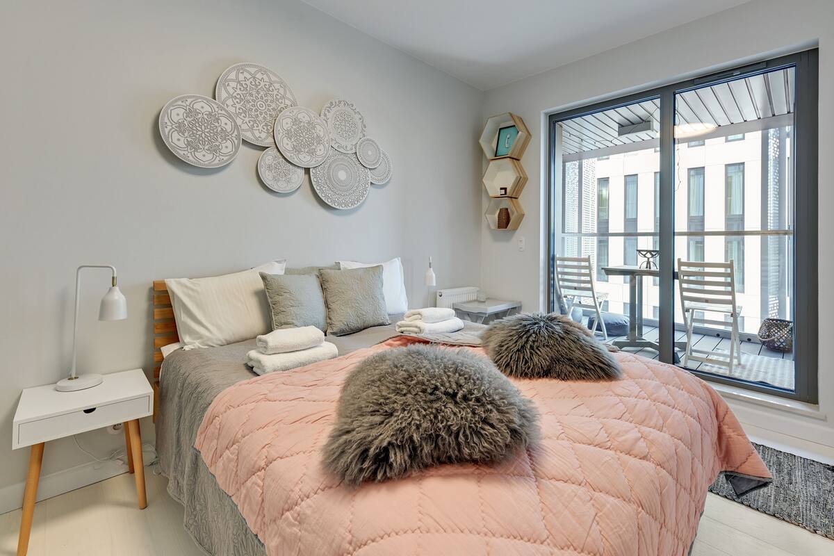 A bedroom with a bed, bedside tables, decorative wall art, and a large window with a view of the outside.