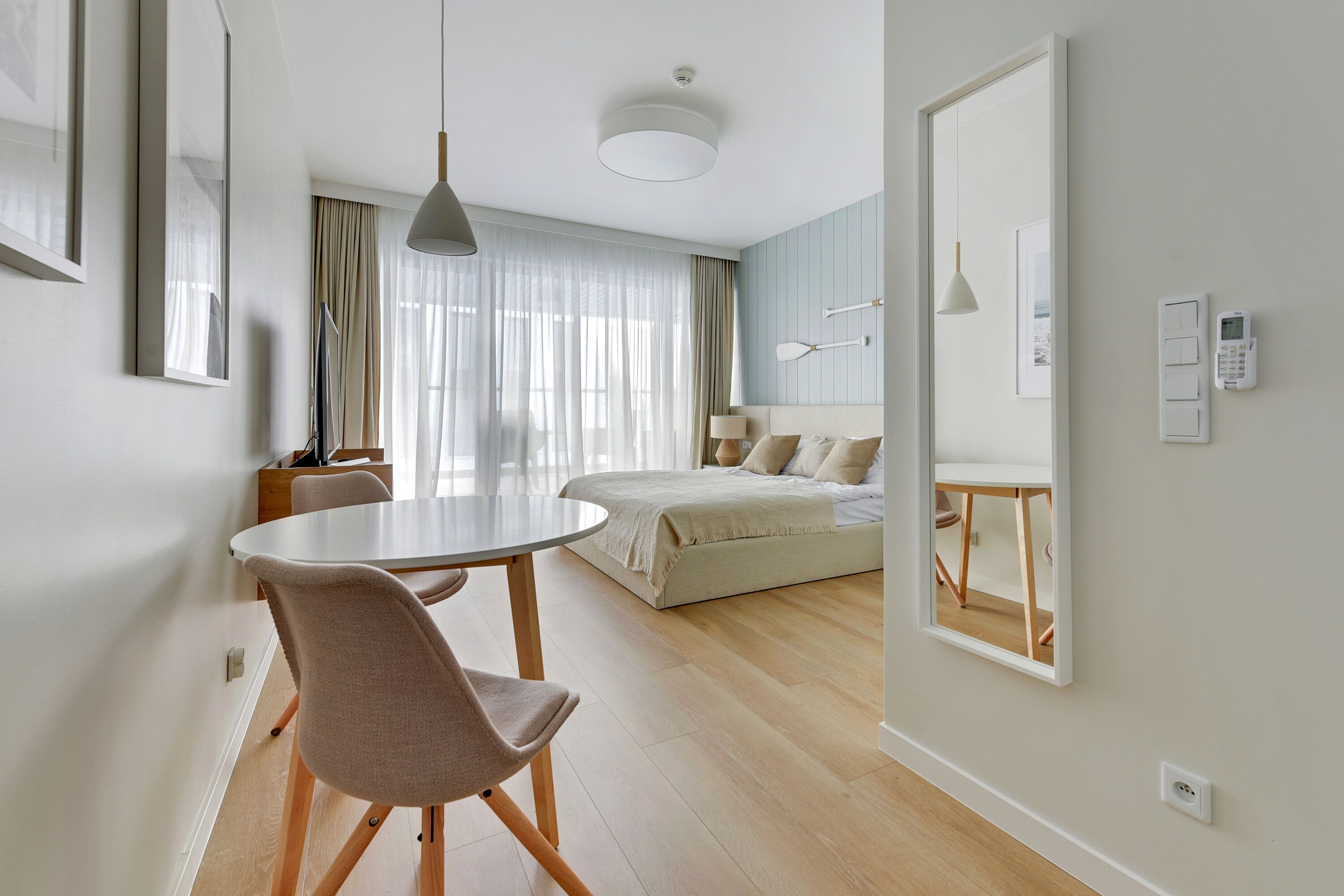 Een moderne hotelkamer met een ronde eettafel, een bed met een witte hoofdbord en een grote spiegel aan de muur.