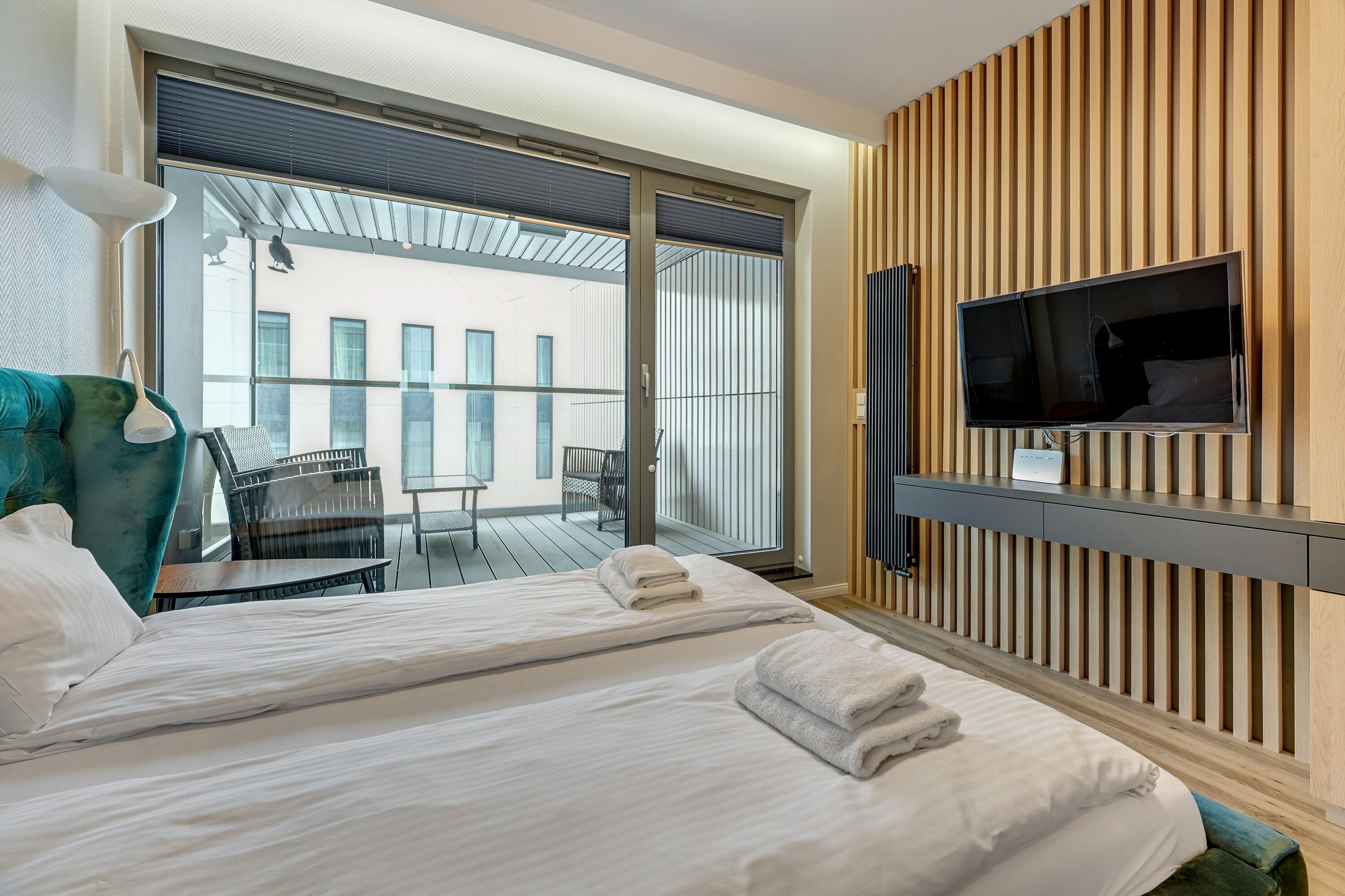 Een hotelkamer met twee bedden, een televisie, een balkon met tafel en stoelen en uitzicht op gebouwen.