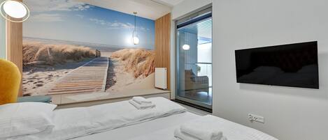 A hotel room with two beds, a large beach mural, a TV, and a window with blinds.