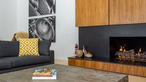 A modern living room with a fireplace, a sofa with patterned cushions, and two abstract wall art pieces. - Apollo 1000 - Space Age Luxury Palm Springs Retreat (Palm Springs)