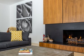 A modern living room with a fireplace, a sofa with patterned cushions, and two abstract wall art pieces.
