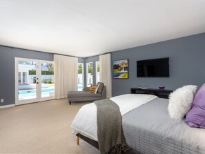 Un dormitorio con una cama, televisión, un cuadro y vista a una piscina.