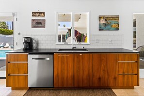 A modern kitchen with a dishwasher, wooden cabinets, a sink, and a window overlooking a pool area.