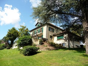 A two-story house with a balcony, surrounded by greenery and trees.