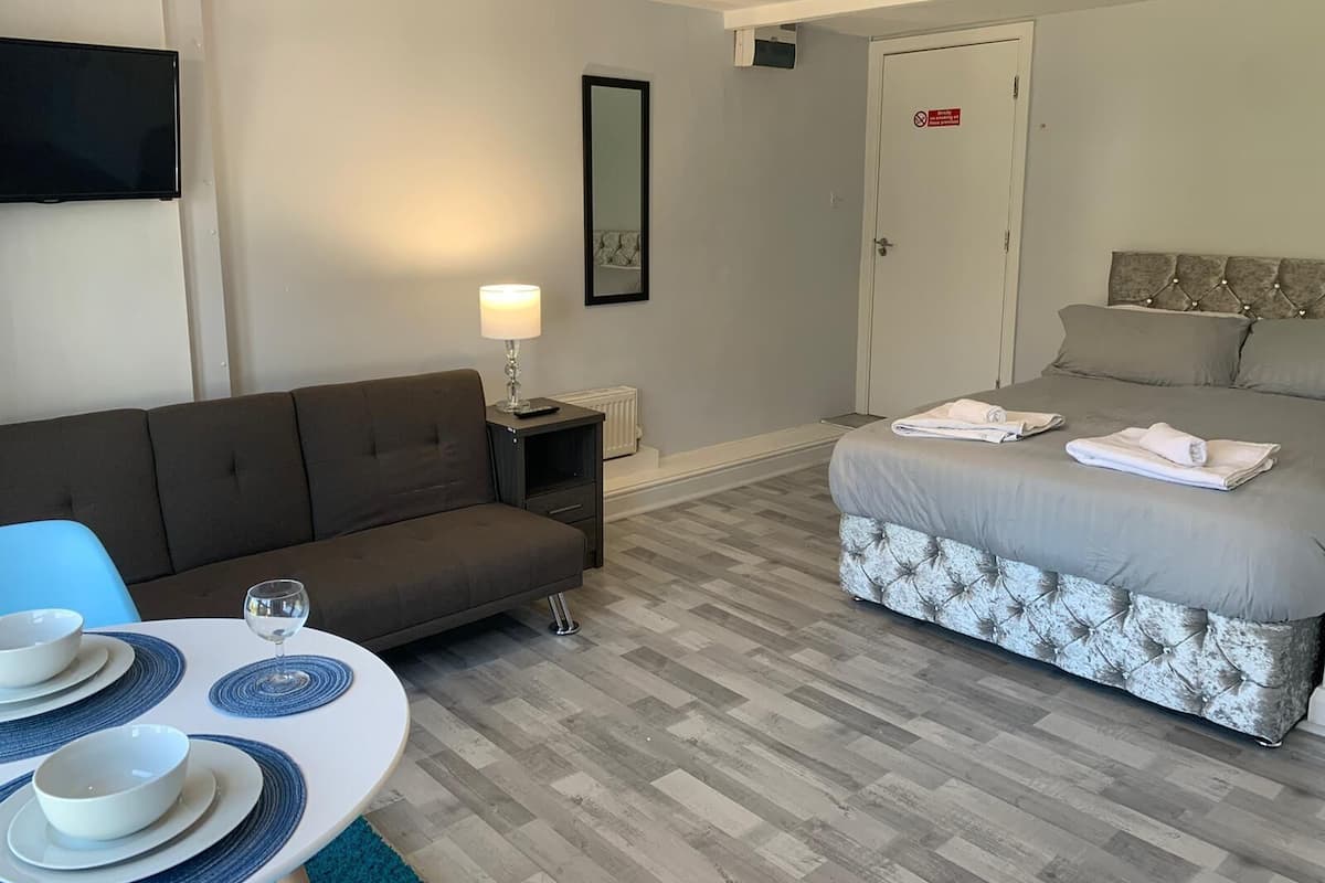 A hotel room with a sofa, a bed with towels, a table with plates and a glass, and a TV on the wall.