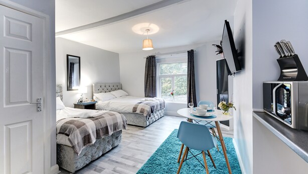 A modern bedroom with two beds, a small dining area, and a TV on the wall. - Grey Stone Studio Apartments (Halifax)