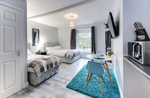 Une chambre moderne avec deux lits, un petit coin repas et un téléviseur fixé au mur.
