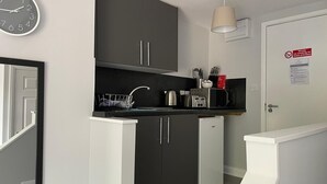 A modern kitchen with dark cabinets, a sink, and a microwave. There is a clock on the wall and a sign prohibiting smoking. - Grey Stone Studio Apartments (Halifax)