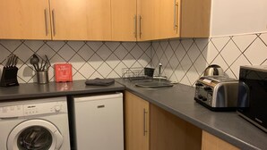 A compact kitchen with a washing machine, a toaster, and a kettle. - Grey Stone Studio Apartments (Halifax)