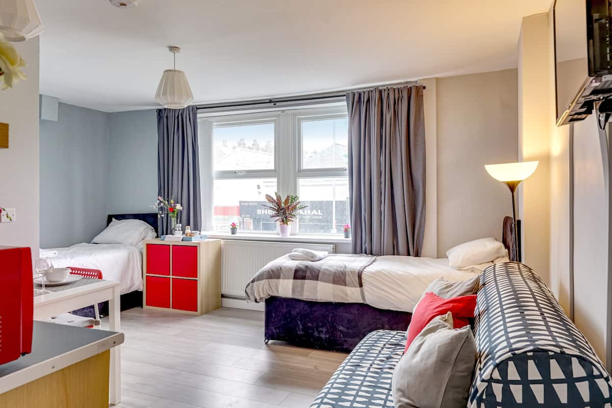 A modern hotel room with a bed, a sofa, a desk, and a window with curtains.