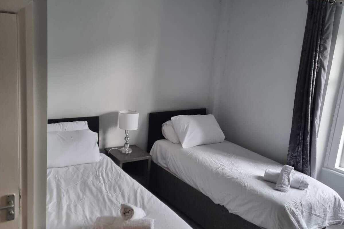 A hotel room with two single beds, a nightstand with a lamp, and a window with curtains.