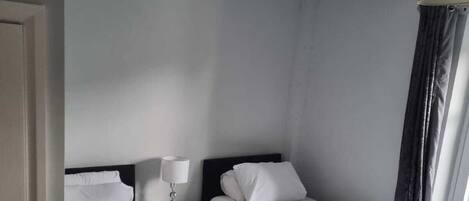 A hotel room with two single beds, a nightstand with a lamp, and a window with curtains.