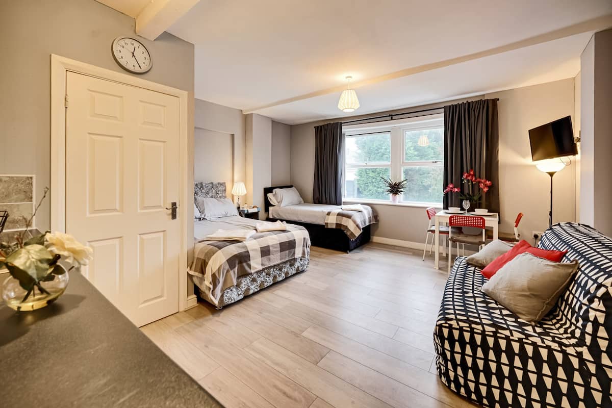 A room with a bed, a sofa, a desk with a chair, a TV, and a window with curtains.