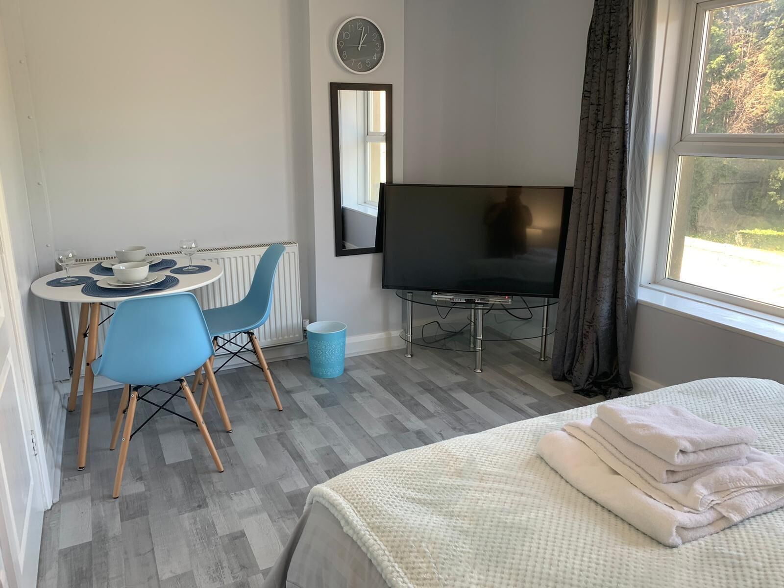 A room with a bed, a TV, a small table with chairs, and a window with curtains.