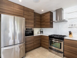 Uma cozinha moderna com eletrodomésticos de aço inoxidável, armários de madeira e um revestimento de azulejos em padrão herringbone.