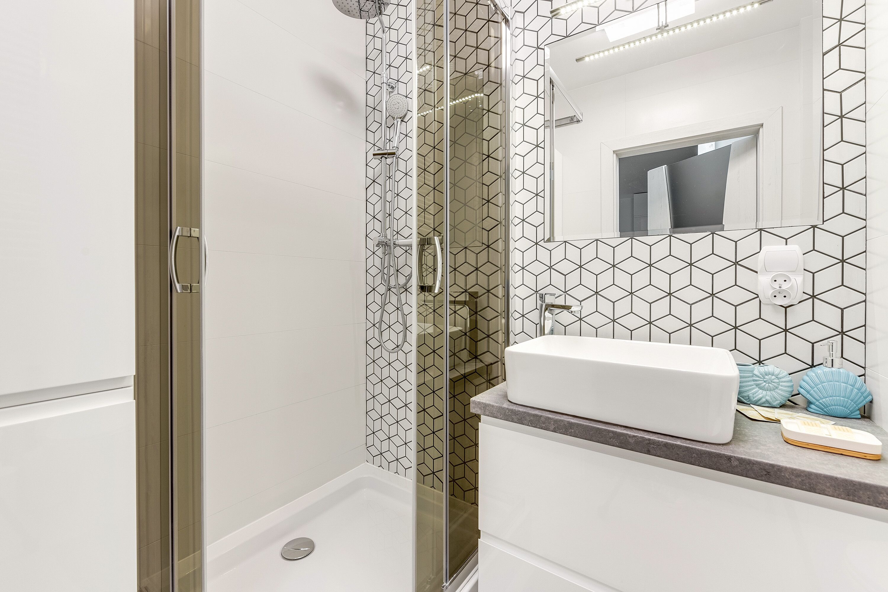 A bathroom with a glass-enclosed shower, a white sink, and a geometric-patterned wall.