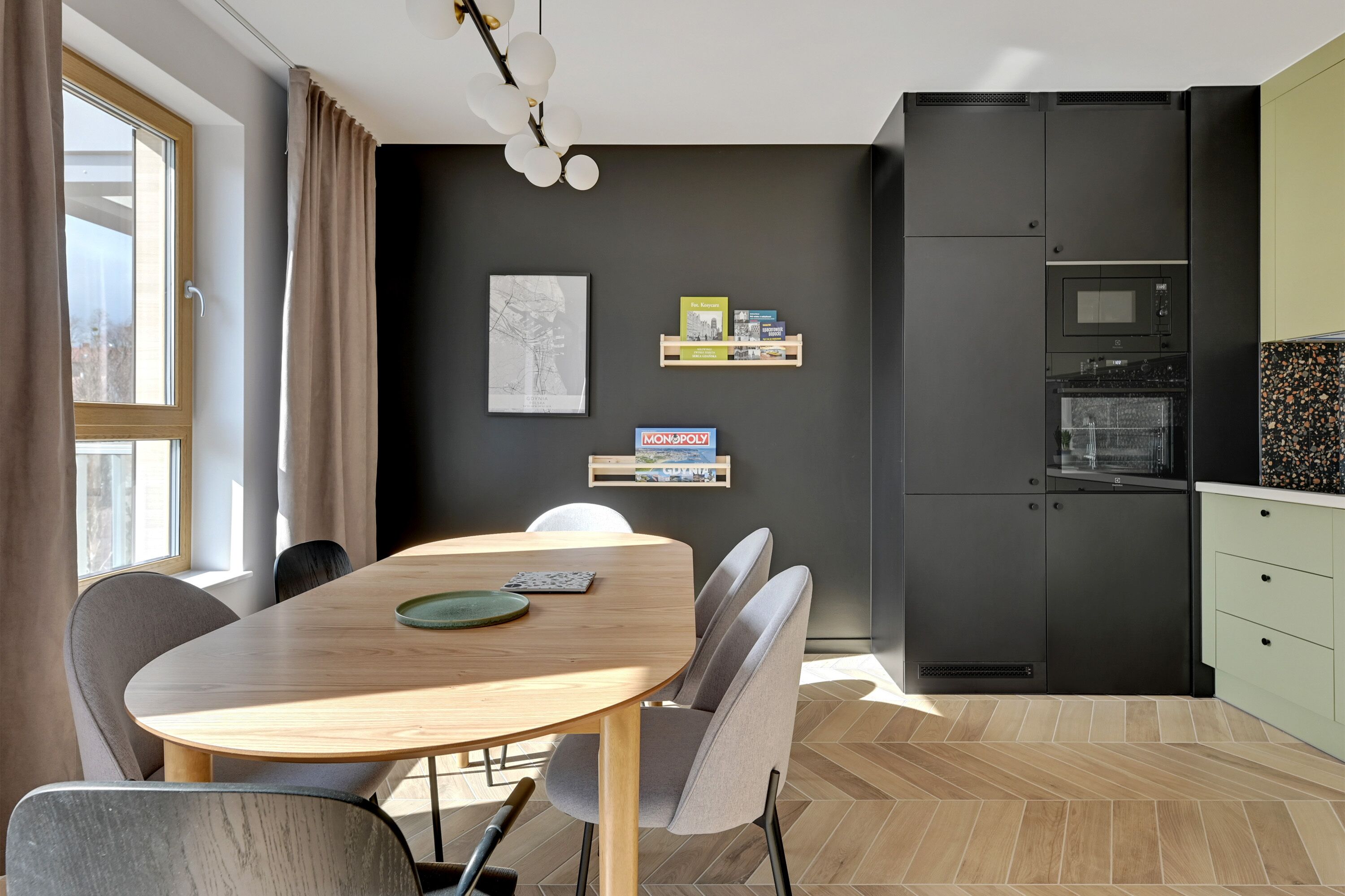 Una cocina moderna con un refrigerador negro, una mesa de comedor de madera con sillas y una pequeña estantería con libros y una caja del juego MONOPOLY.
