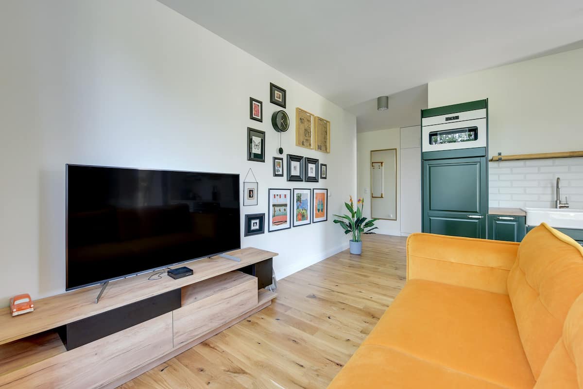 Een moderne woonkamer met een flatscreen televisie, een houten tv-meubel en een fel oranje bank.