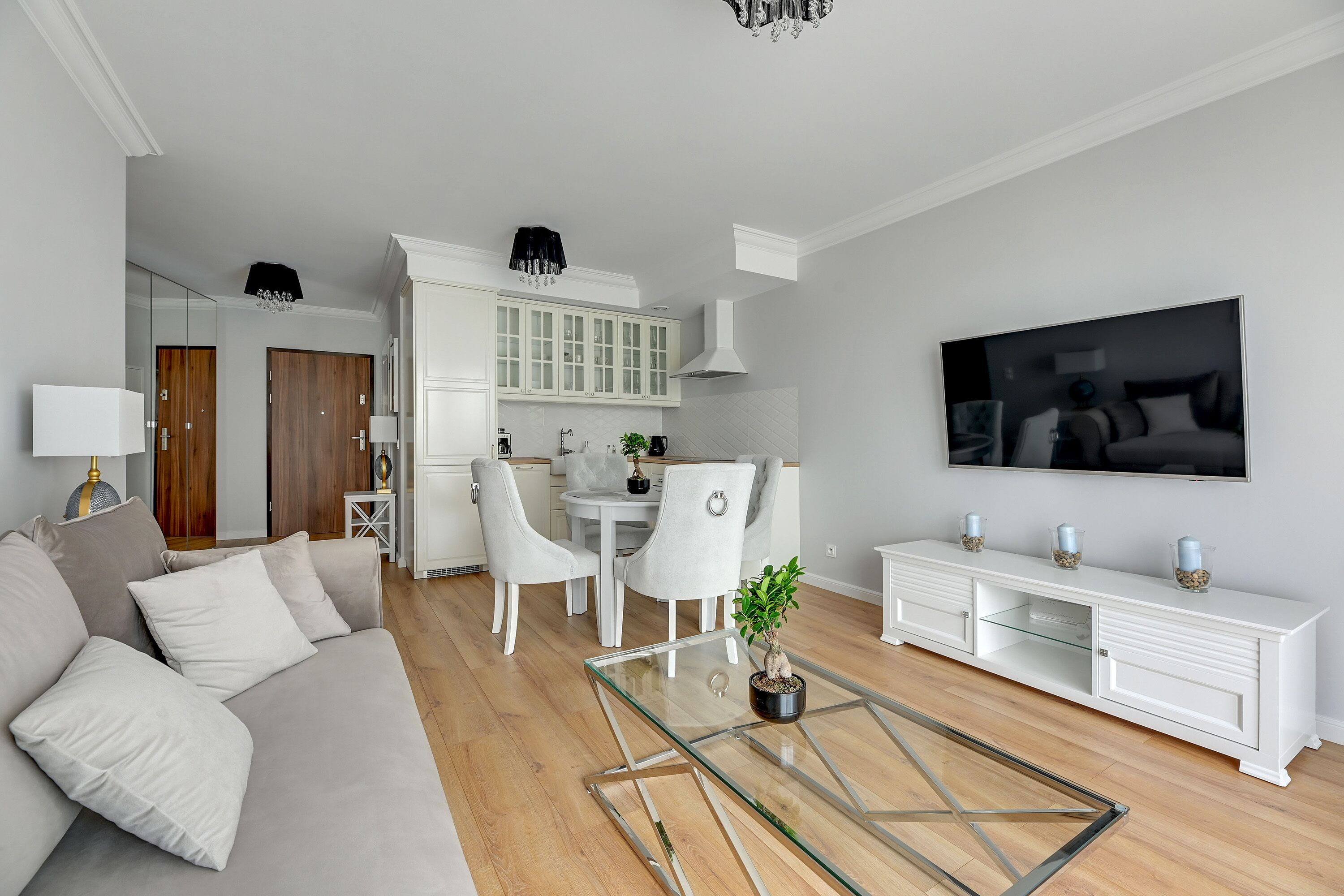 Un salon moderne avec une table basse en verre, un canapé, un téléviseur et un coin repas comprenant des chaises et des meubles de rangement.