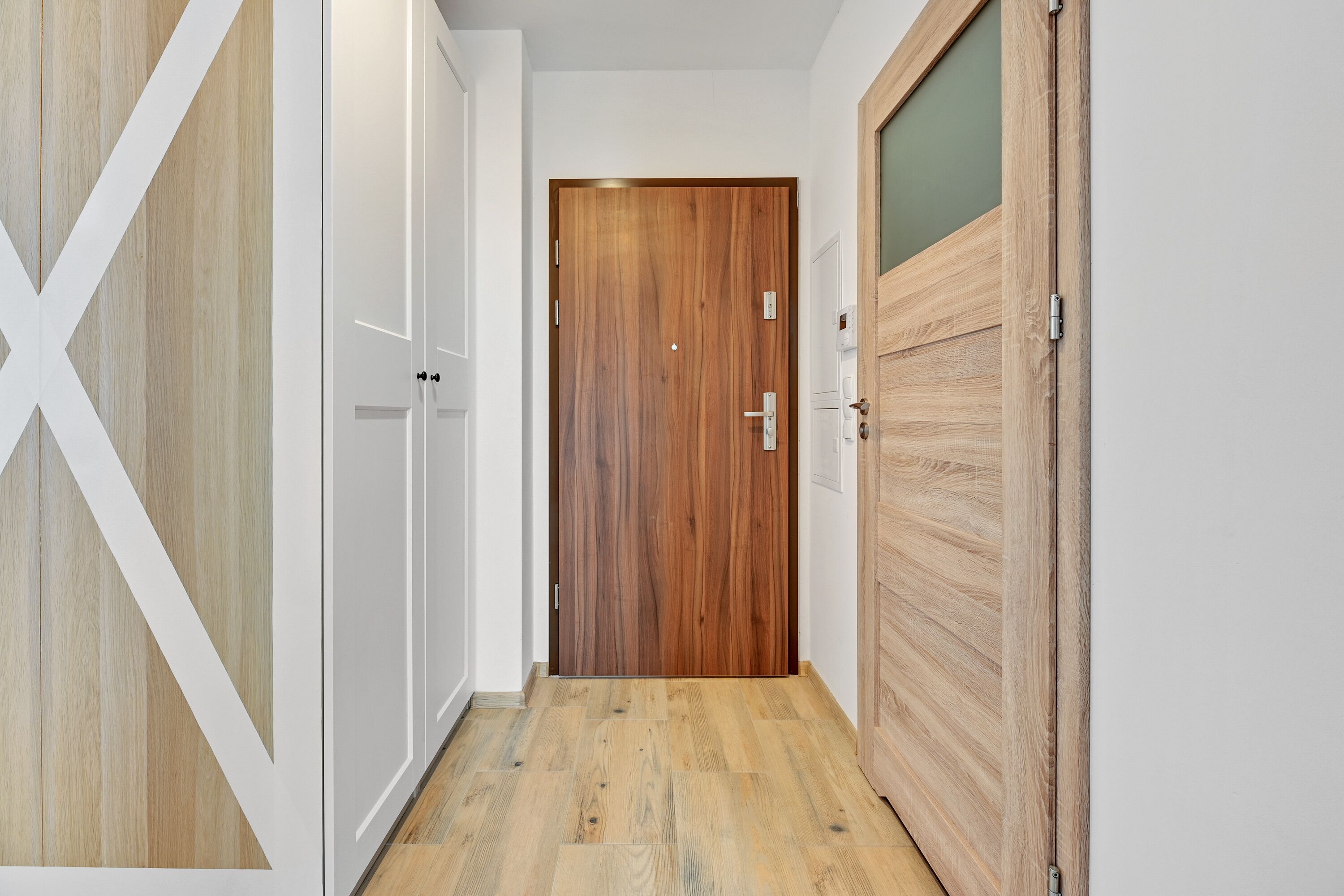 A hallway with wooden flooring, white walls, and a wooden door at the end.