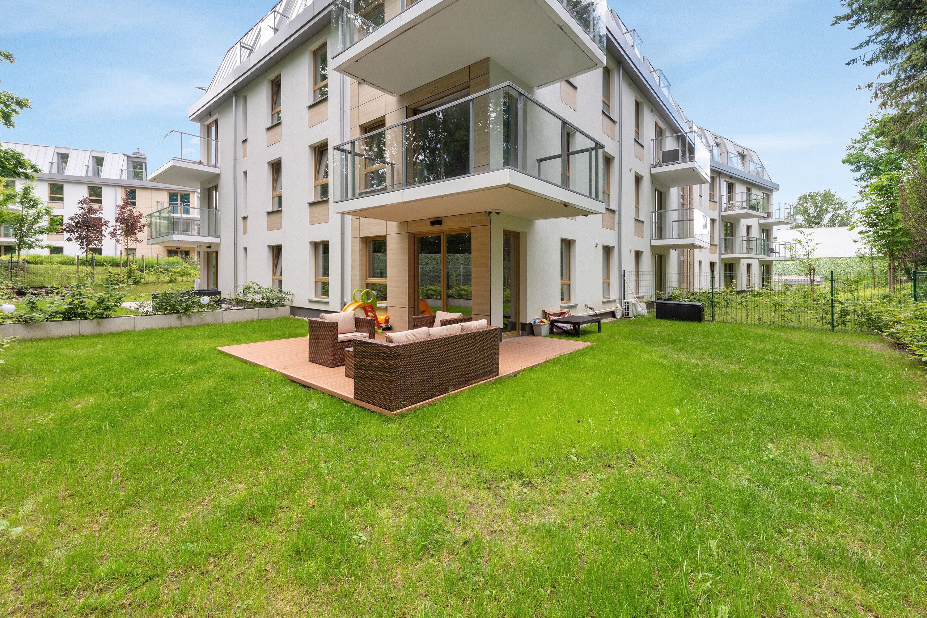 Un immeuble résidentiel moderne à plusieurs étages, doté d’un balcon, d’une pelouse bien entretenue et d’un espace extérieur aménagé pour s’asseoir.