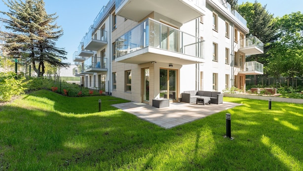 A modern multi-story building with large glass windows, outdoor seating, and a well-maintained lawn.