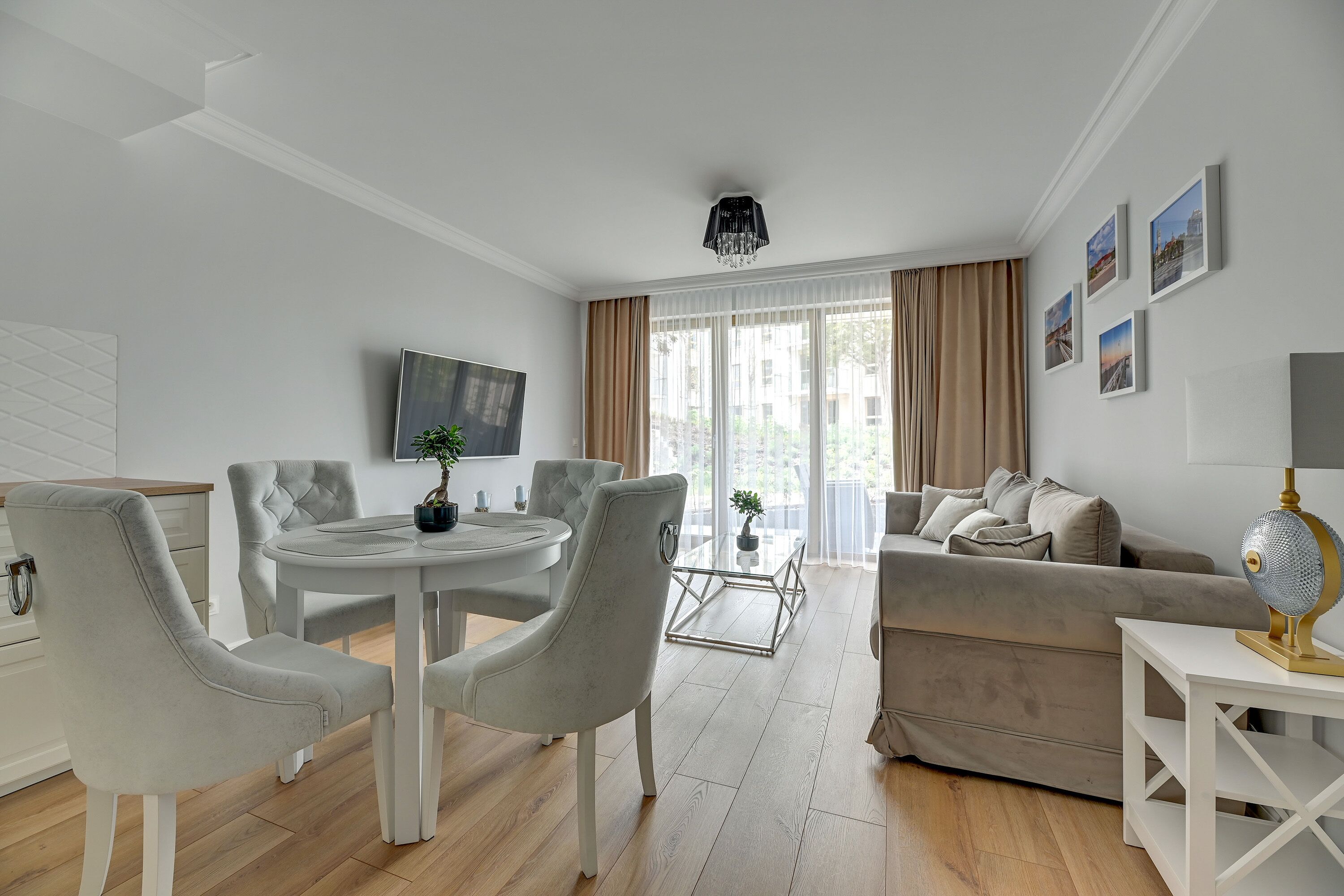 A modern living room with a white sofa, grey armchairs, a round dining table, and a TV mounted on the wall.