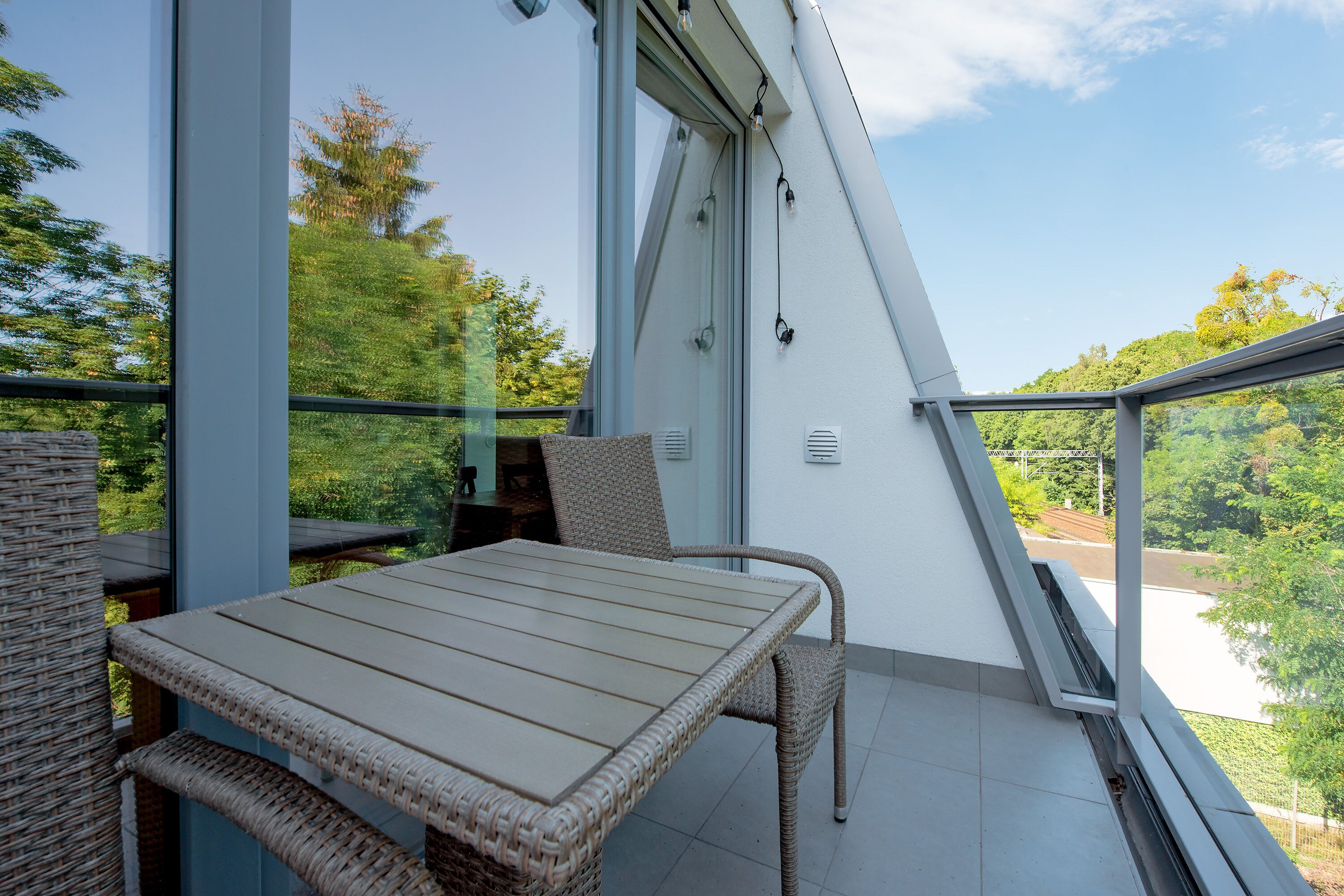 Un balcon avec une table et des chaises, une porte vitrée et une vue sur la verdure.