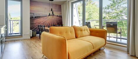 A modern living room with a large sofa, a dining area with chairs, and a mural of a pier.